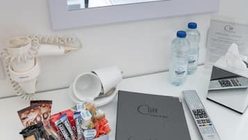 A hotel room with a bed, a mirror, a desk with toiletries, a hairdryer, a remote control, and a guest information booklet.