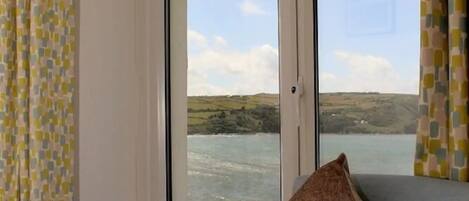 Ein Zimmer mit großem Fenster und Blick auf ein Gewässer und Hügel.