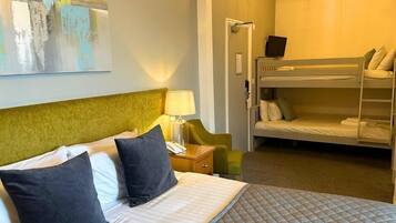 A hotel room with a single bed, a bunk bed, a bedside table with a lamp, and a painting on the wall.