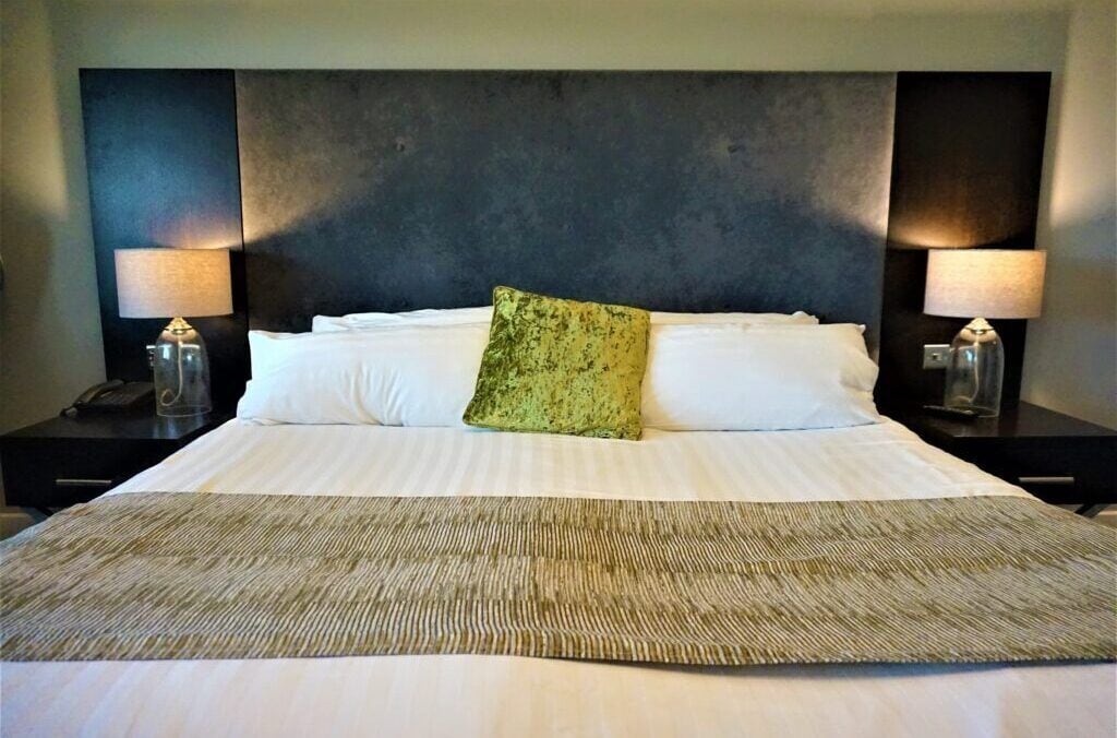 A hotel room with a large bed, two bedside lamps, and a textured throw blanket.