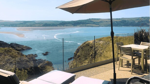 A seaside terrace with a view of the ocean, a table, chairs, and an umbrella. - The Cliff Hotel & Spa (Cardigan)