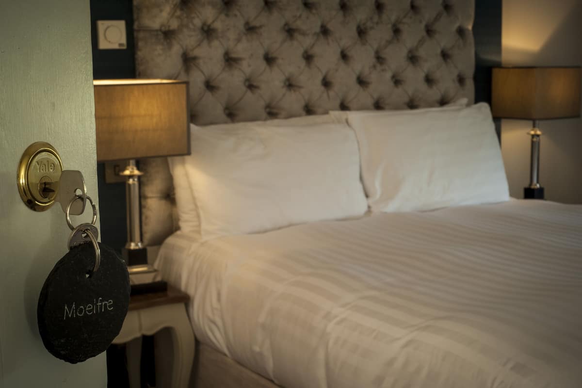 A hotel room with a tufted headboard, white bedding, bedside lamps, and a Yale keychain on the door.