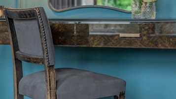 A chair with a dark wooden frame and a grey upholstered seat, positioned in front of a blue wall with a mirror reflecting a window view.