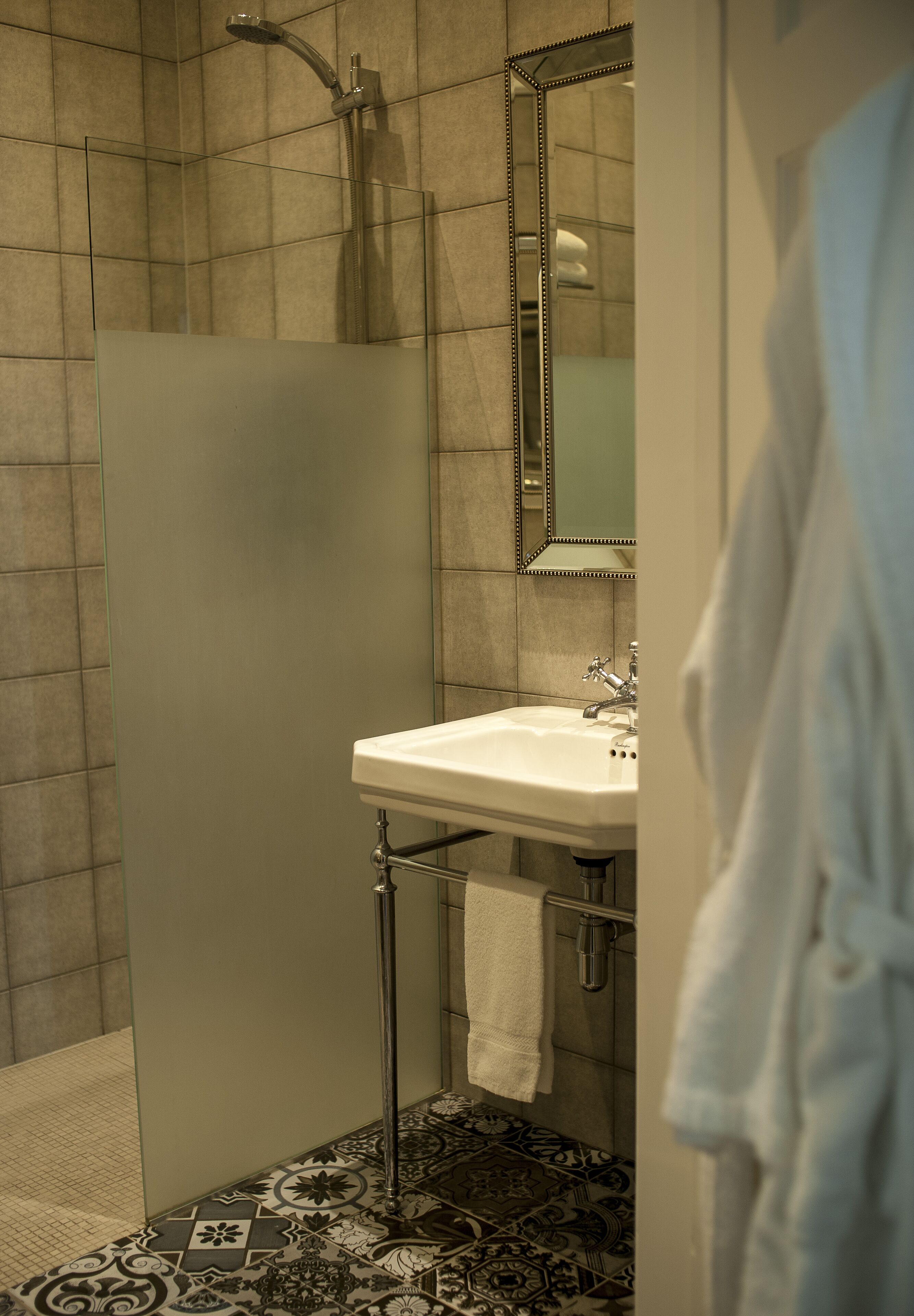 Une salle de bain avec une douche à parois de verre, un lavabo blanc et un carrelage au sol.