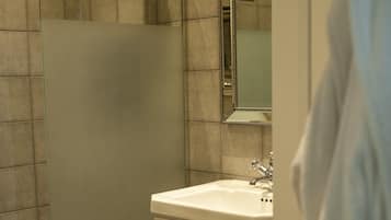 Une salle de bain avec une douche à parois de verre, un lavabo blanc et un carrelage au sol.