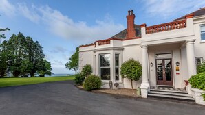 A stately building with a prominent entrance, large windows, and a well-maintained lawn. - Mansion House Llansteffan (Carmarthen)