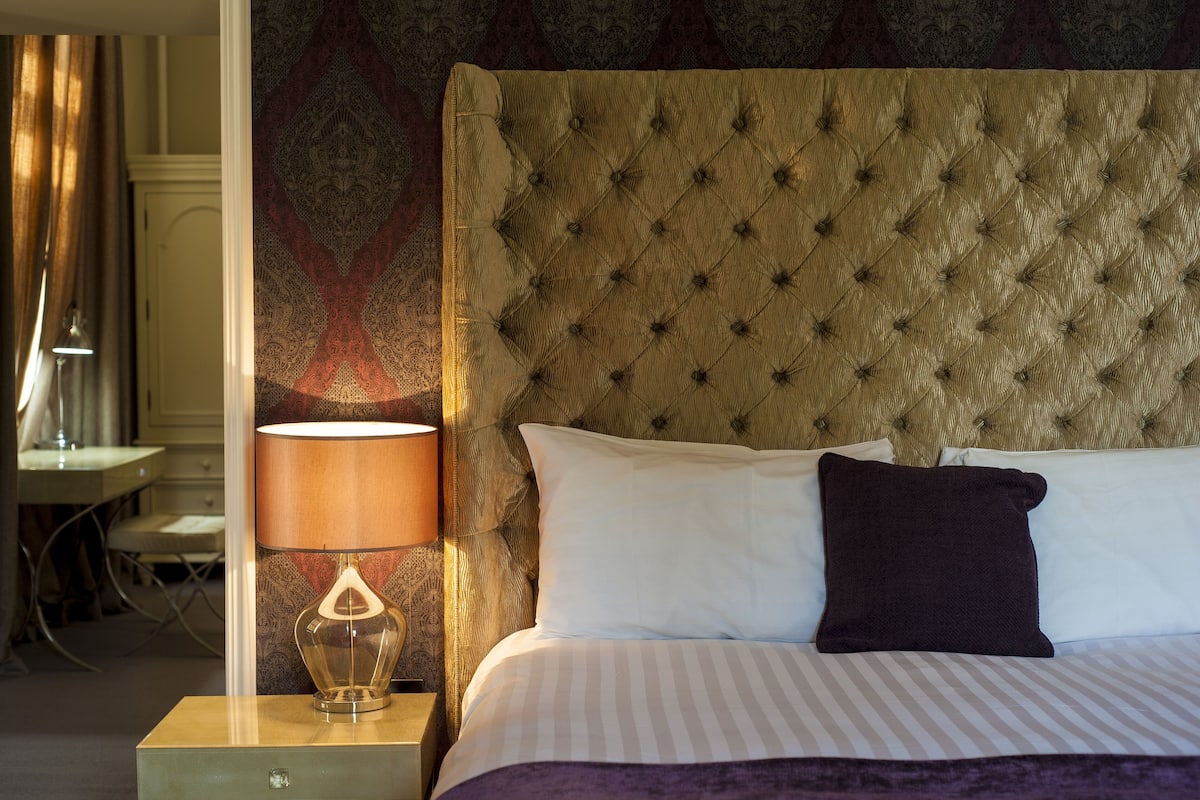A neatly made bed with a tufted headboard, a bedside lamp, and a patterned wall.