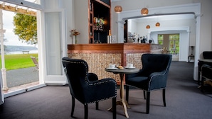 A bar area with two chairs and a table, a bar counter with bottles, and a view of the outdoors. - Mansion House Llansteffan (Carmarthen)