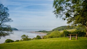 A grassy hill with a bench overlooking a beach and the sea. - Mansion House Llansteffan (Carmarthen)