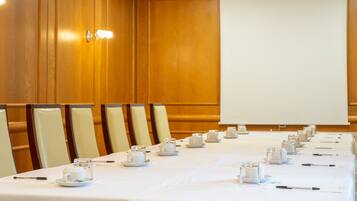 A conference room with a long table set for a meeting, equipped with chairs, a projector screen, and a whiteboard.