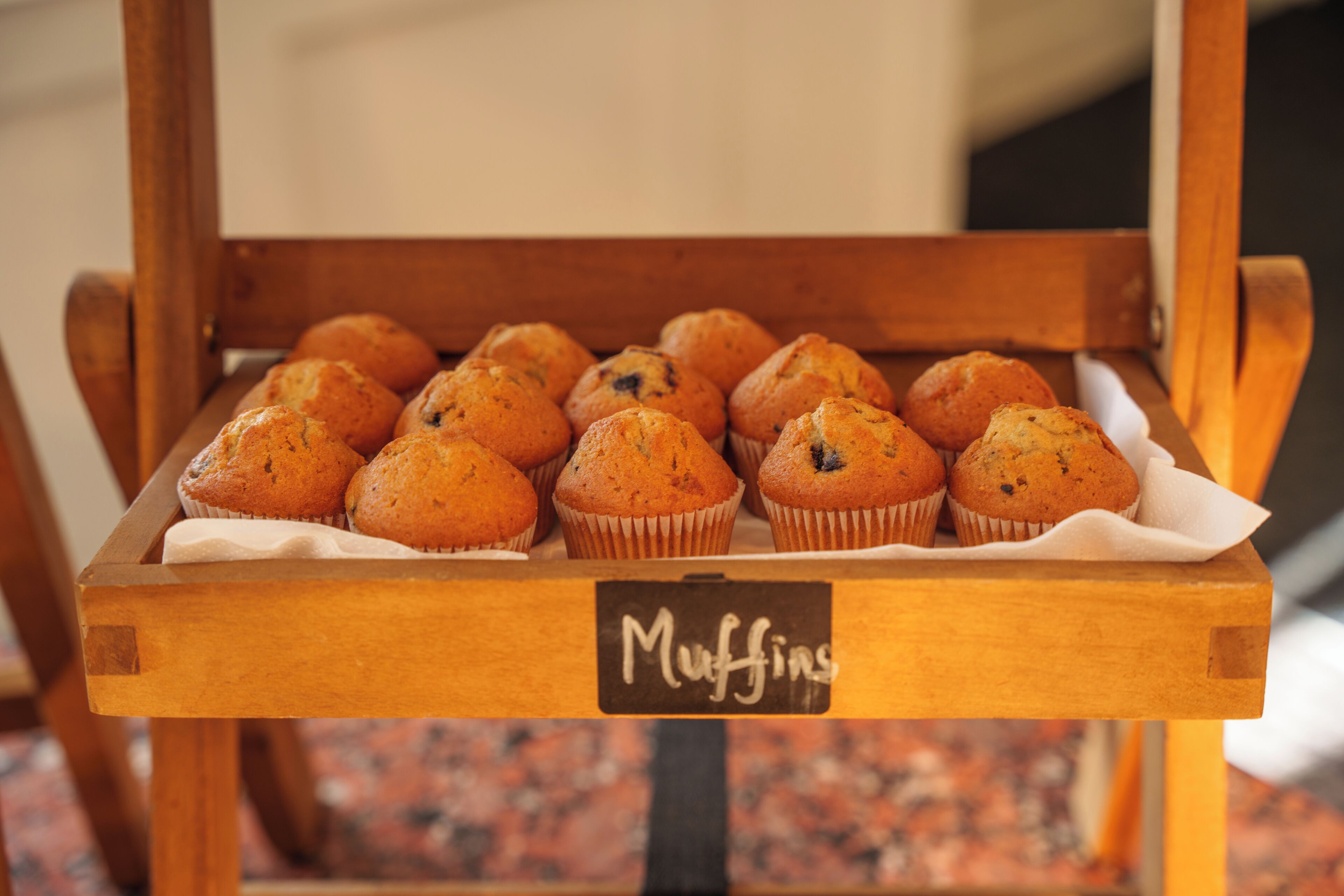 A wooden tray with muffins labeled "Muffins" on a table.
