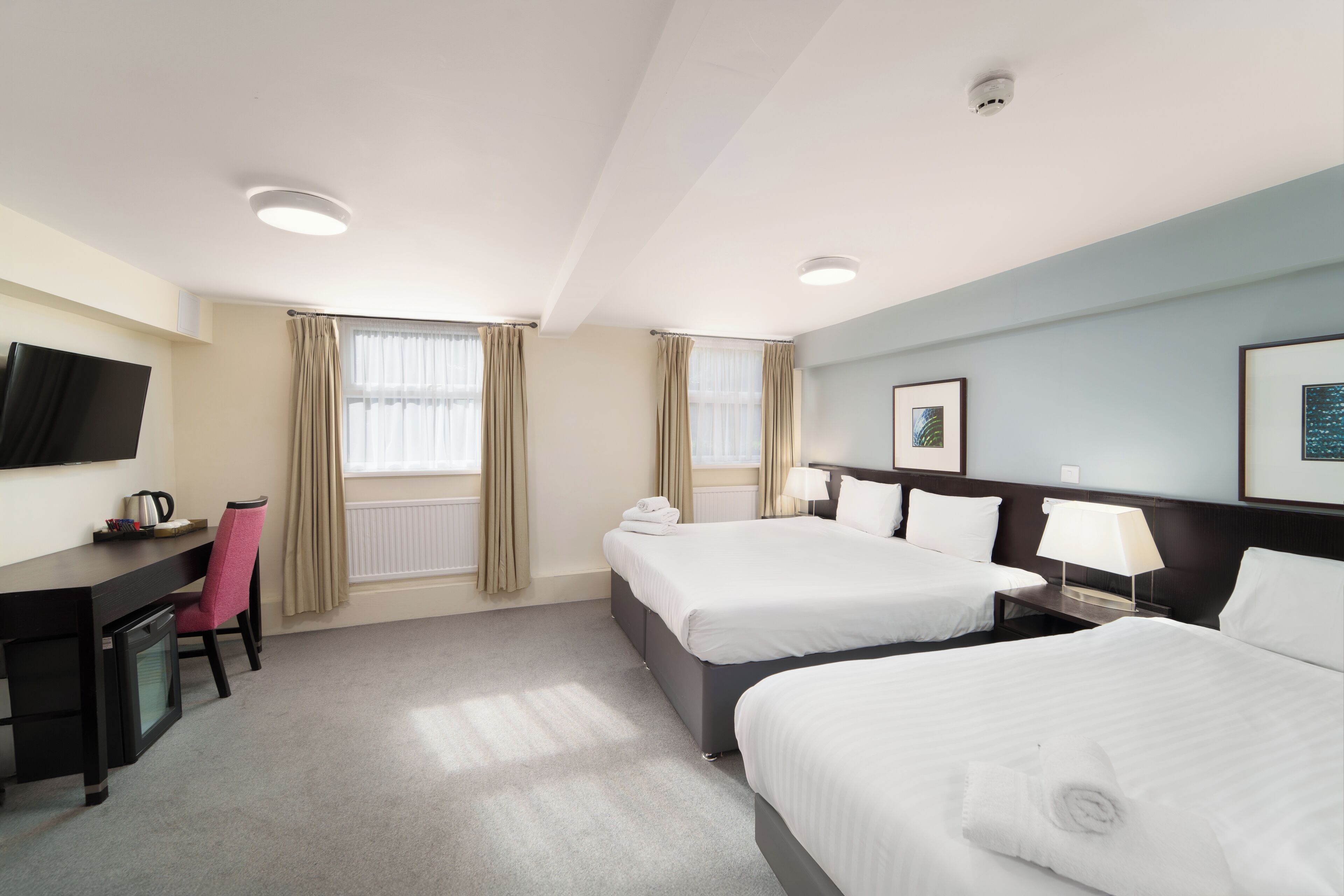 A hotel room with two beds, a desk, a chair, a TV, and a window with curtains.