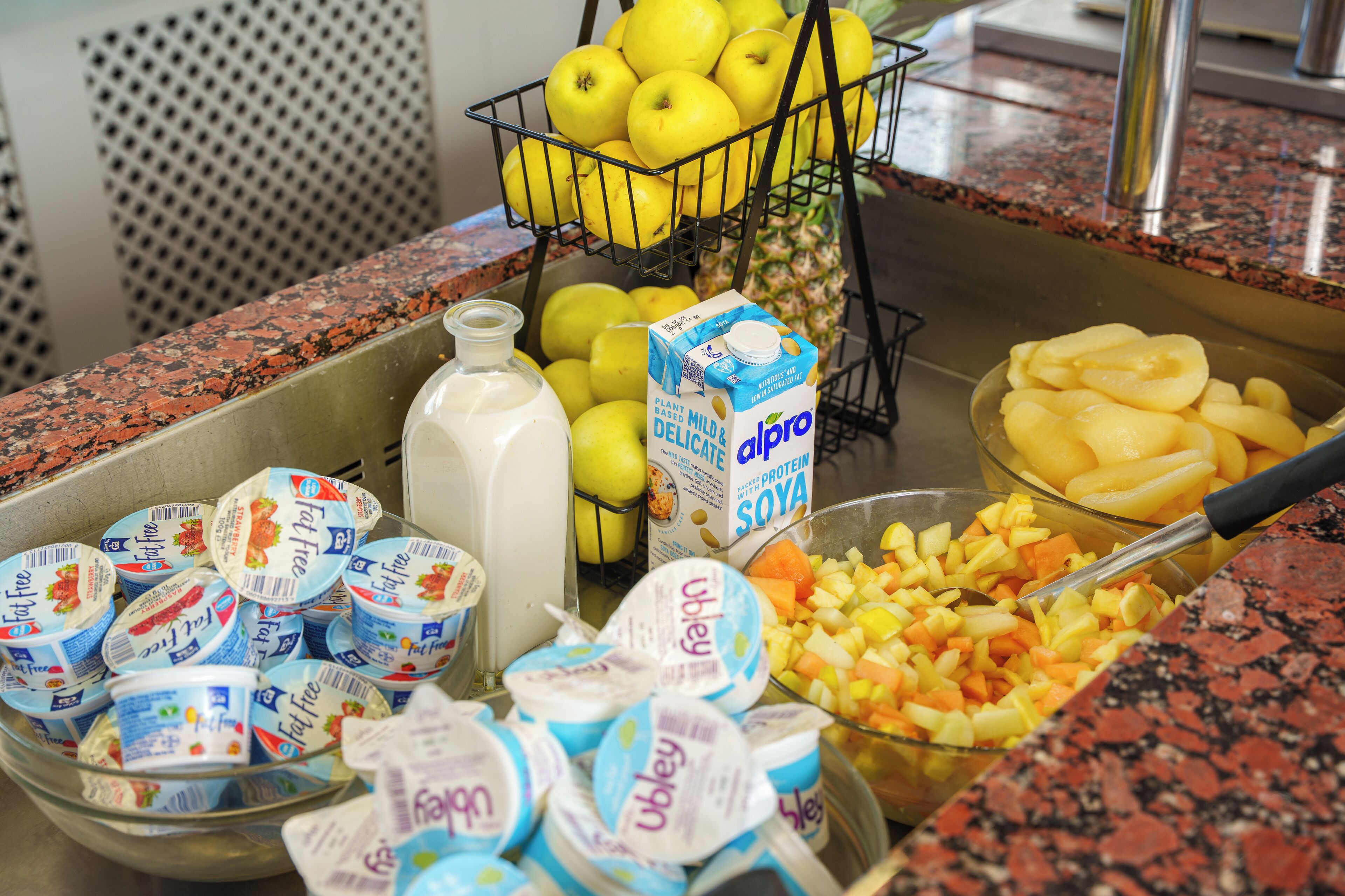A buffet with yogurt, apples, pineapple, and diced fruit.