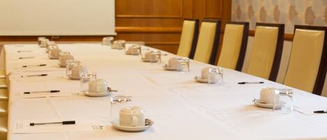 Una mesa de conferencias dispuesta con tazas, platitos y bolígrafos, con sillas alineadas en un lado.