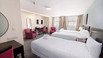 Quarto de hotel com duas camas, uma escrivaninha, uma cadeira, uma TV e um espelho grande.