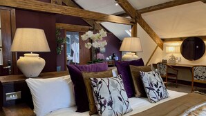A bedroom with a large bed, two bedside lamps, a wooden ceiling, and a view of a bathroom. - The Cawdor (Llandeilo)