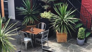 An outdoor patio with a wooden table and chairs, surrounded by potted plants. - The Cawdor (Llandeilo)
