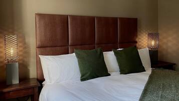 A neatly made bed with white linens and two green pillows, a brown headboard, and two bedside tables with decorative lamps.