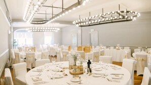 A banquet hall with round tables set for a formal event, featuring white tablecloths, glassware, and floral centerpieces. - The Cawdor (Llandeilo)