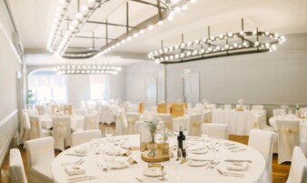 A banquet hall with round tables set for a formal event, featuring white tablecloths, glassware, and floral centerpieces.