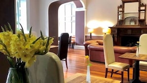 A hotel lobby with a wooden reception desk, leather seating, and a vase of yellow flowers. - The Cawdor (Llandeilo)
