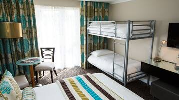 Una habitación de hotel con literas, un escritorio con lámpara, una silla y una pequeña mesa con revistas.