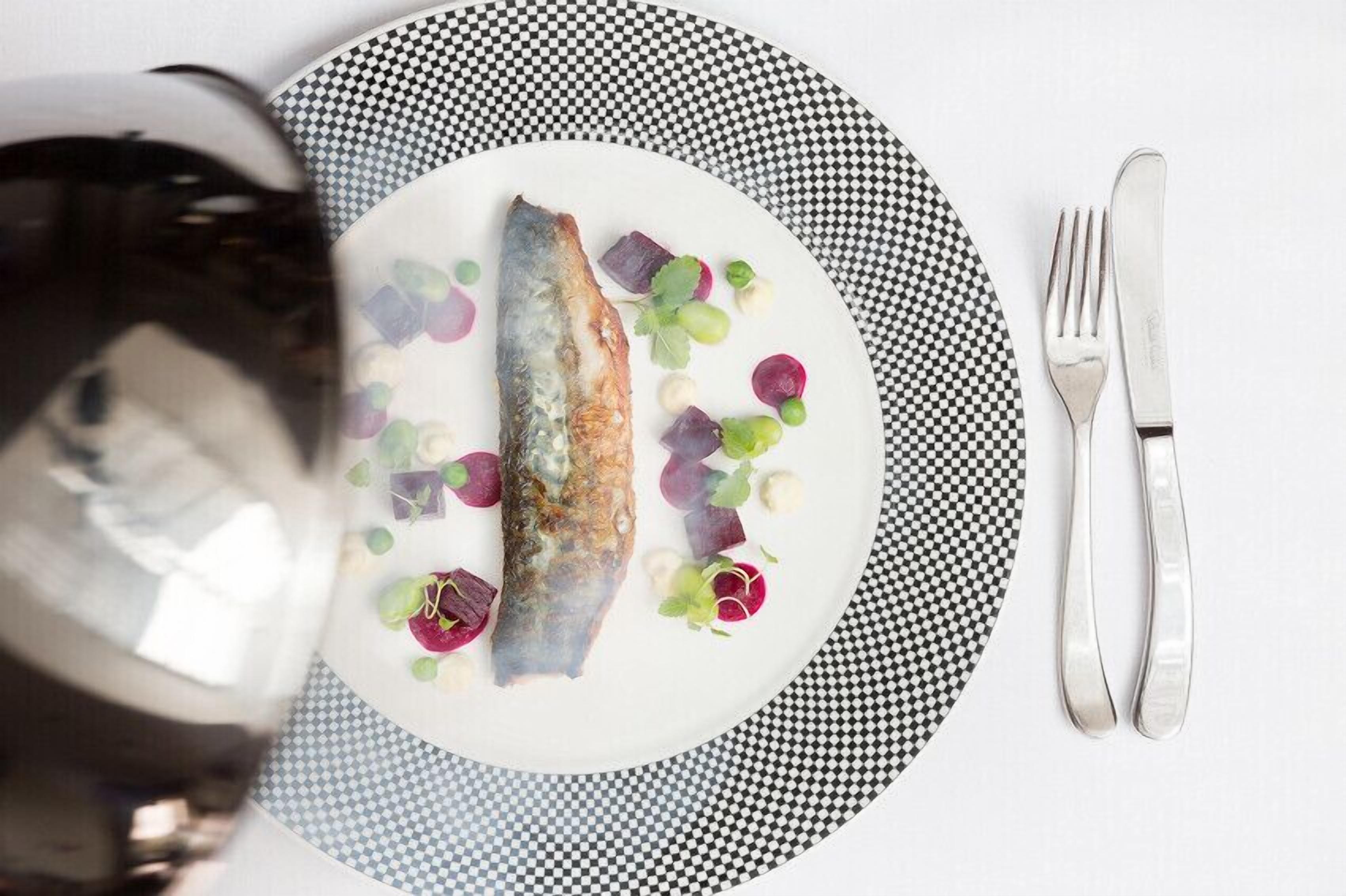 A plate of food with a fish, vegetables, and a glass of red wine.