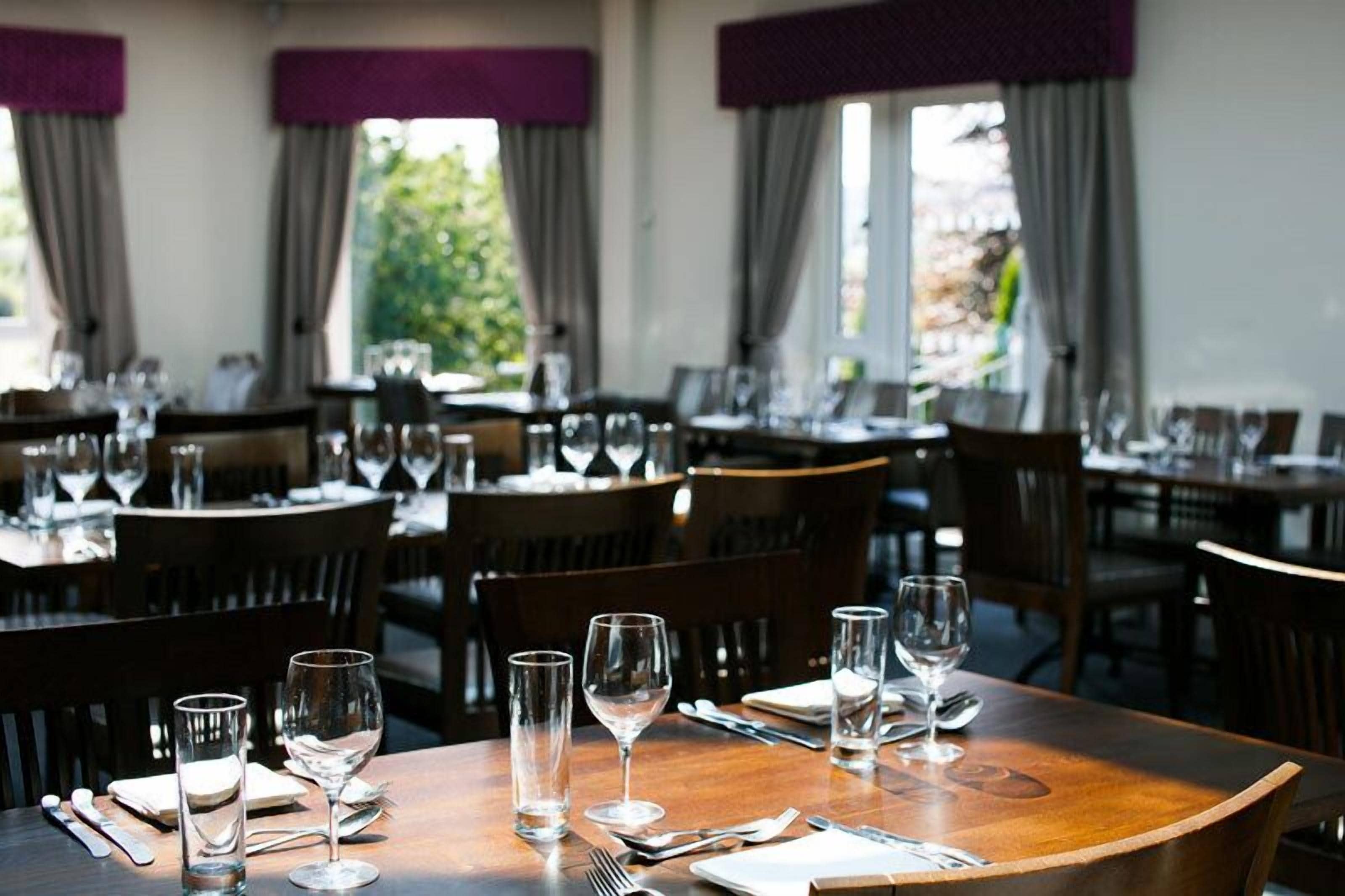 Un restaurant où de nombreuses tables sont dressées pour le service, chacune étant agrémentée de verres à vin et de couverts.