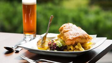 Un plato con pescado frito, papas fritas, una cerveza en un vaso y una ensalada como guarnición sobre una mesa con tenedor y cuchara.