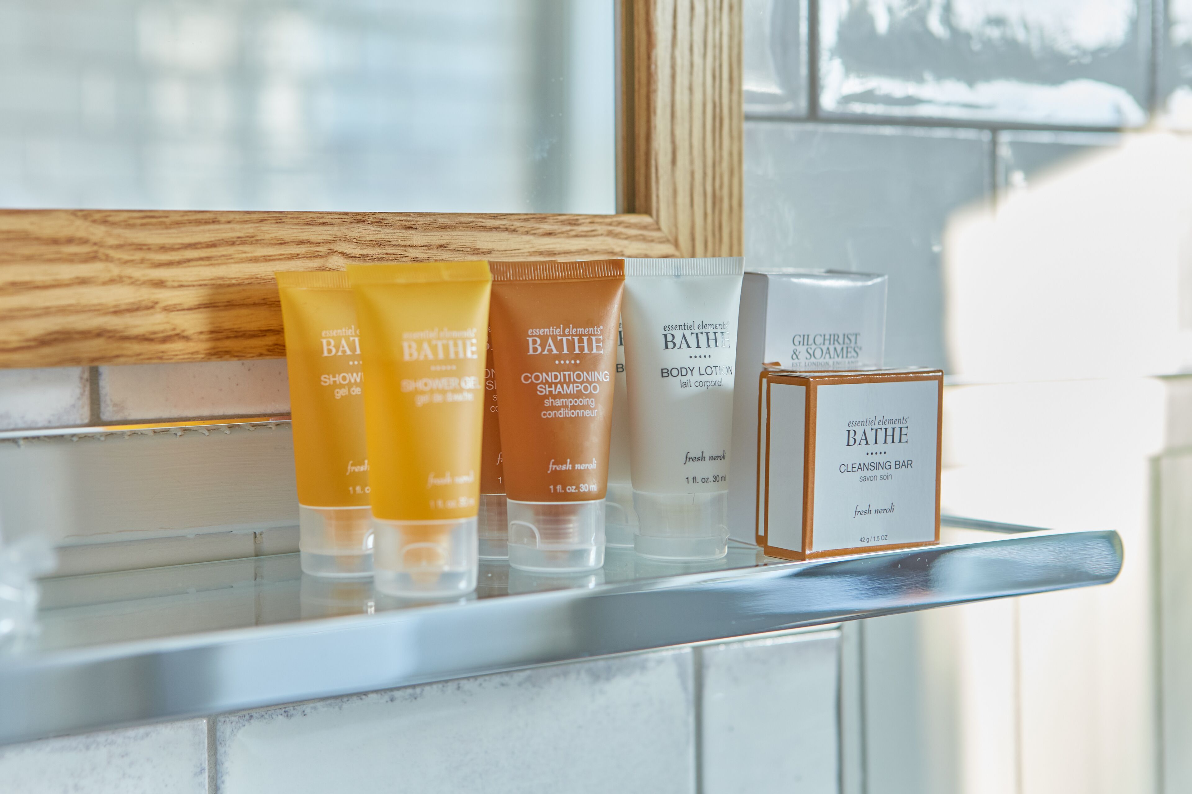 A bathroom shelf with various Bath products including a shower gel, conditioning shampoo, body lotion, and a cleansing bar.