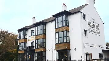 Un edificio de dos plantas con ventanas grandes y un letrero que dice 'Anglesey Arms Pub, Dining and Rooms'.