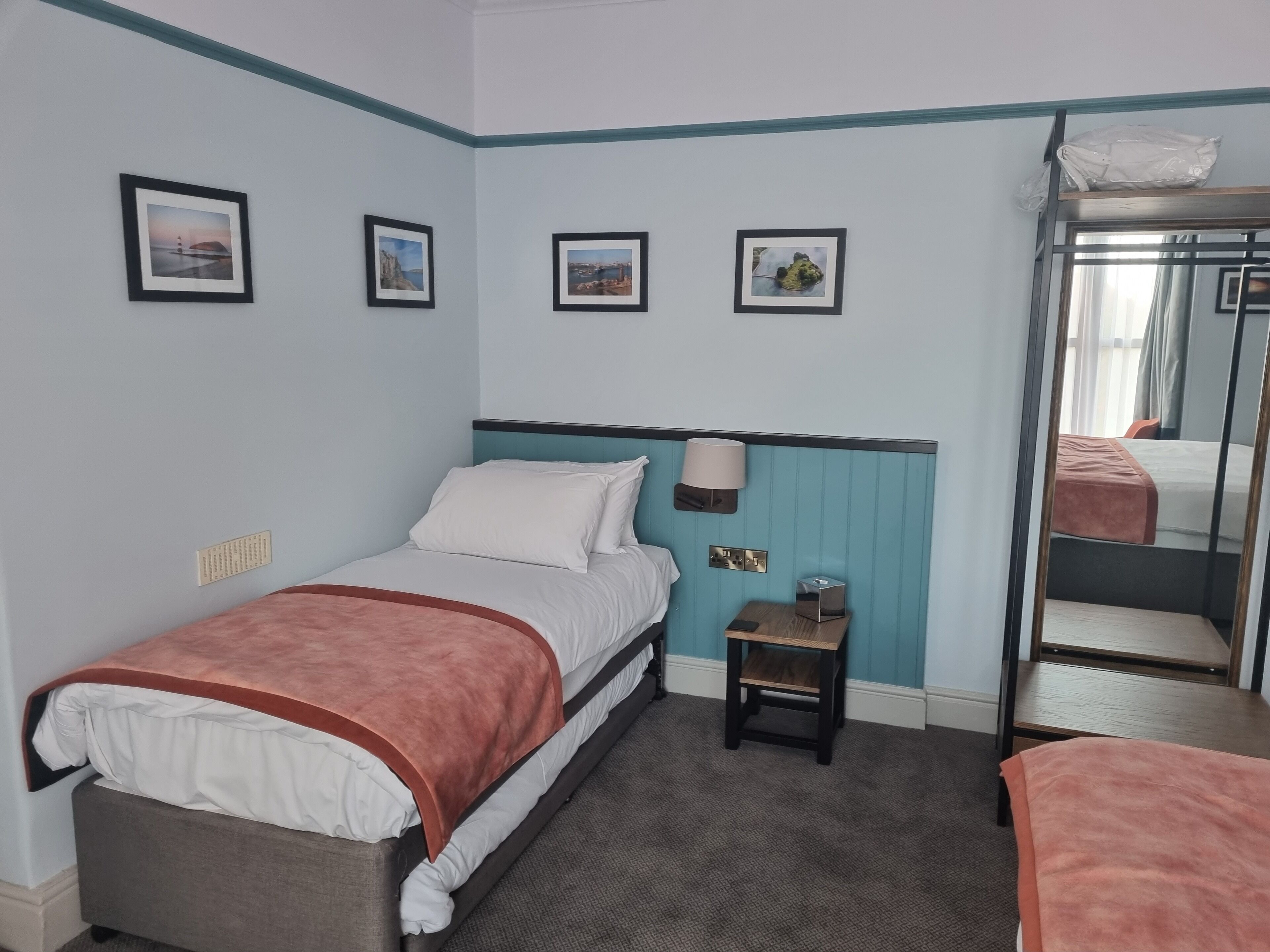 Een hotelkamer met een bed, een klein nachtkastje, een lamp en een spiegel.