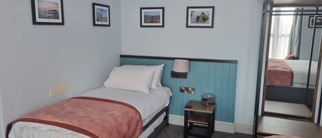 A hotel room with a bed, a small bedside table, a lamp, and a mirror.