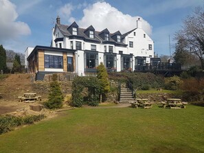 A large, modern two-story building with a stone foundation, multiple windows, and a well-maintained lawn with picnic tables. - The Anglesey Arms (Menai Bridge)