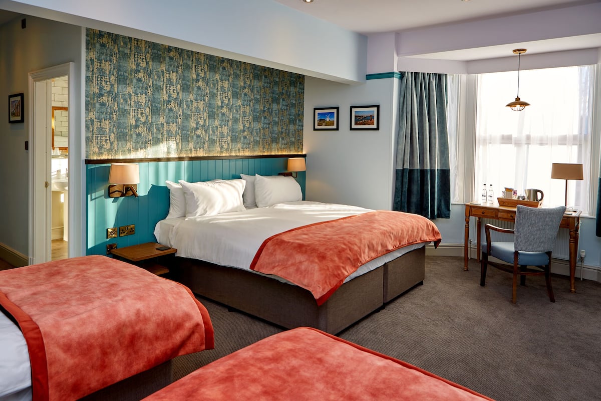 A hotel room with a large bed, two bedside tables, a desk with a chair, and a view of the outdoors.