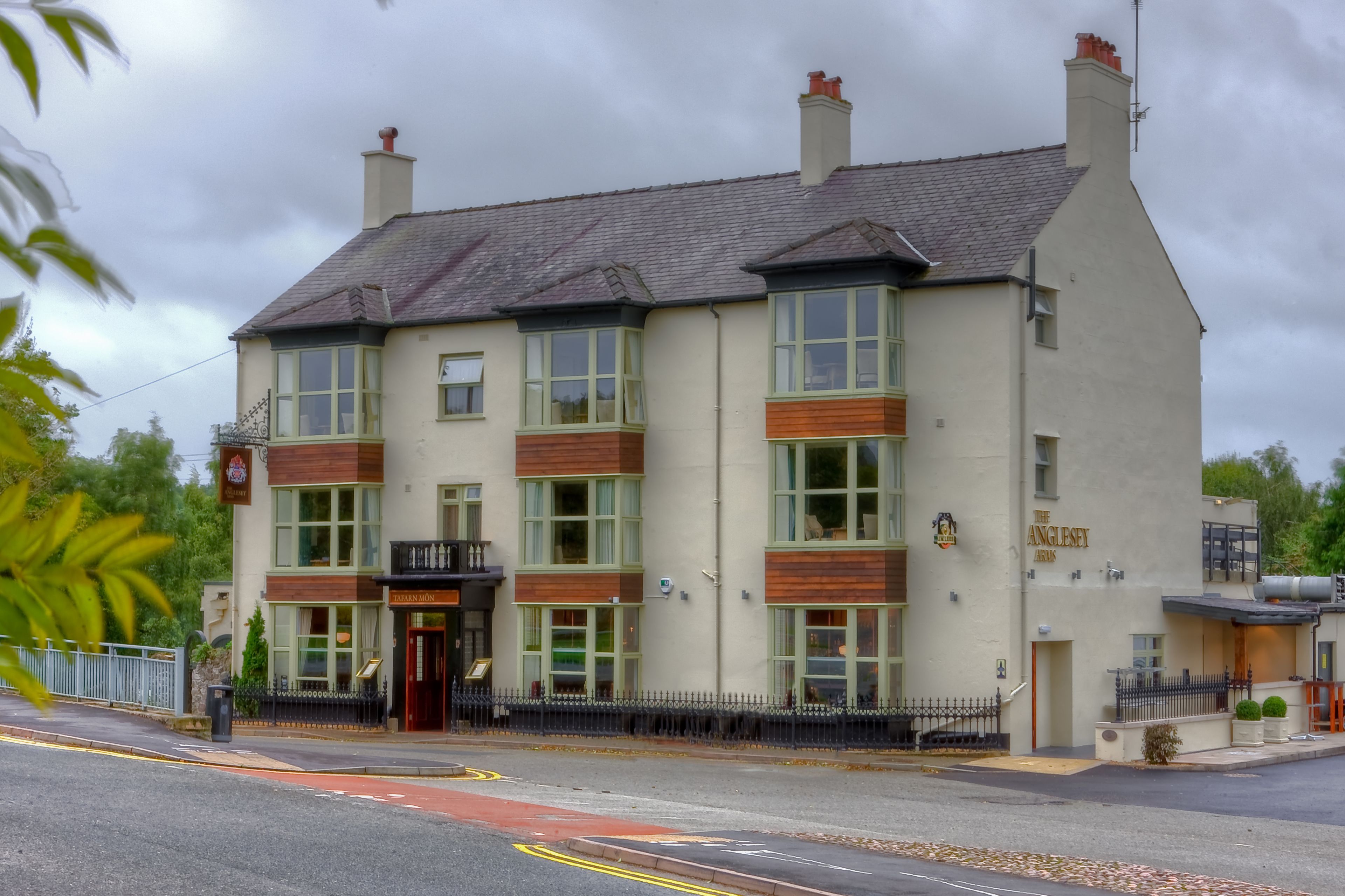 Un edificio de dos pisos con fachada tradicional, que cuenta con ventanas grandes y un letrero que dice 'The Anglesey Arms'.