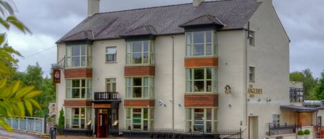 Un edificio de dos pisos con fachada tradicional, que cuenta con ventanas grandes y un letrero que dice 'The Anglesey Arms'.