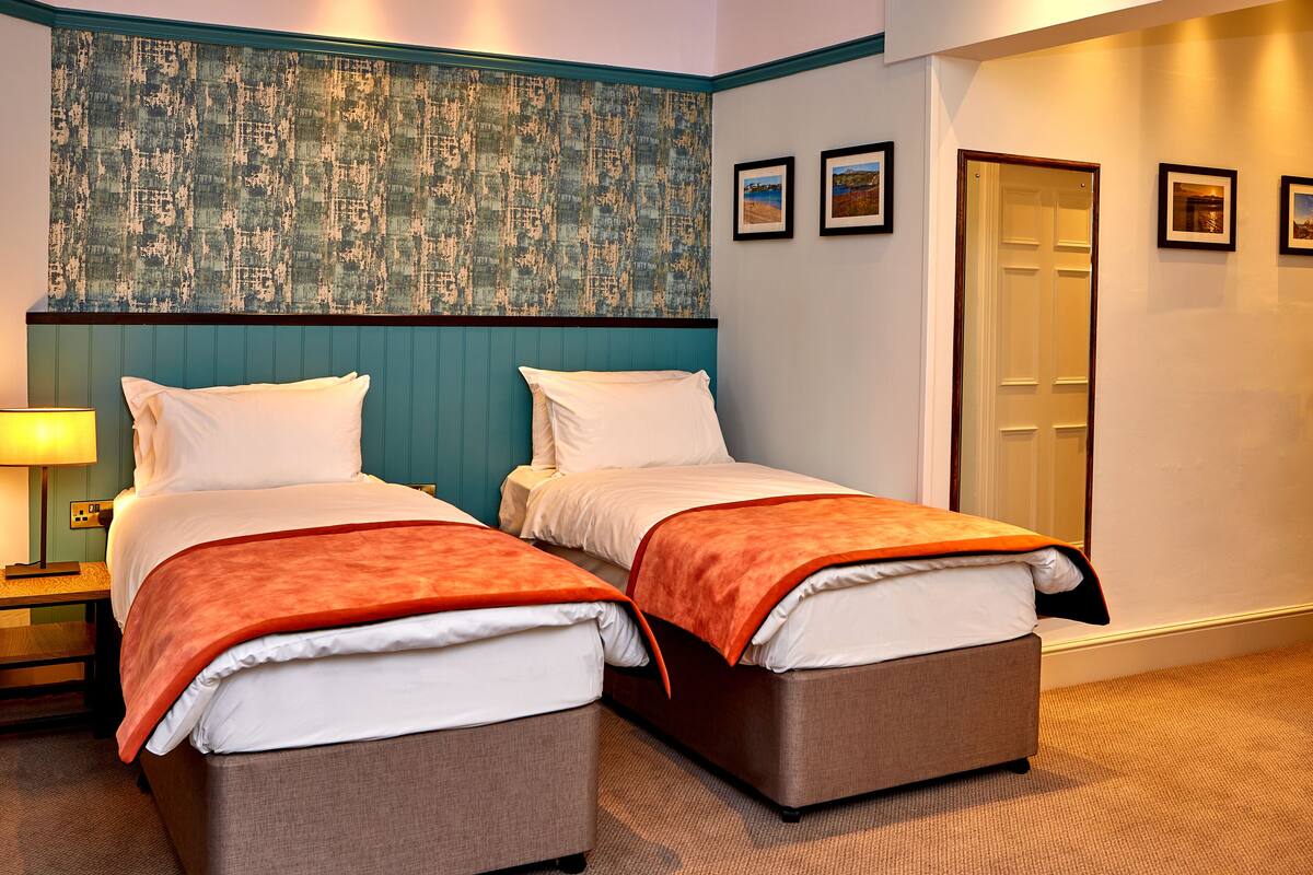 A hotel room with two beds, a nightstand, a lamp, and a door.
