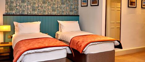 A hotel room with two beds, a nightstand, a lamp, and a door.