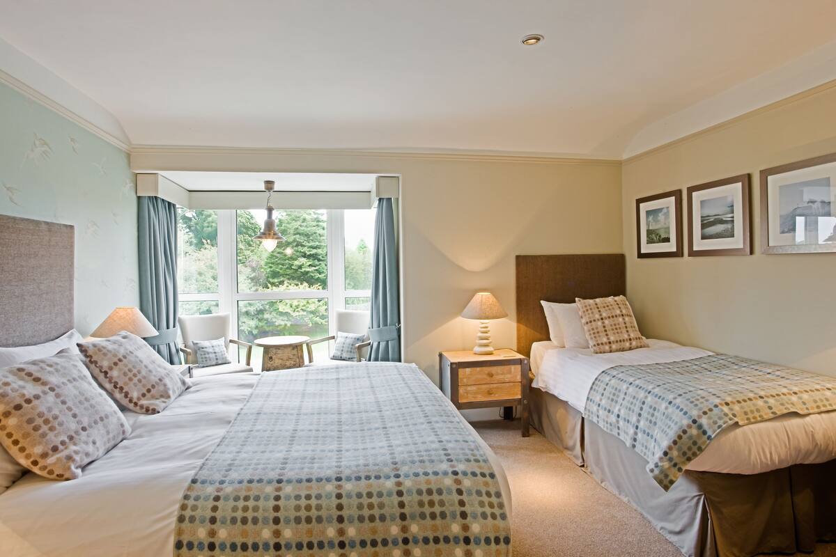 A hotel room with two beds, a small table, a chair, and a window with curtains.