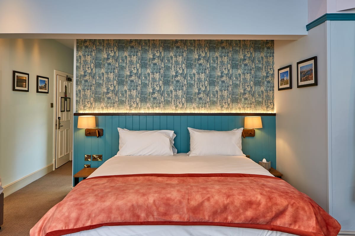 A hotel room with a large bed, two bedside lamps, a blue headboard, and a red throw blanket.