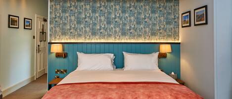 Una habitación de hotel con una cama grande, dos lámparas de noche, un cabecero azul y una manta roja.