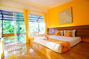 A hotel room with a large bed, a wooden headboard, a window with curtains, and a view of greenery outside. - Aurora Resort (Kanchanaburi)