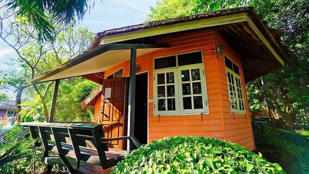 A small wooden cabin with a porch, surrounded by lush greenery. - Aurora Resort (Kanchanaburi)