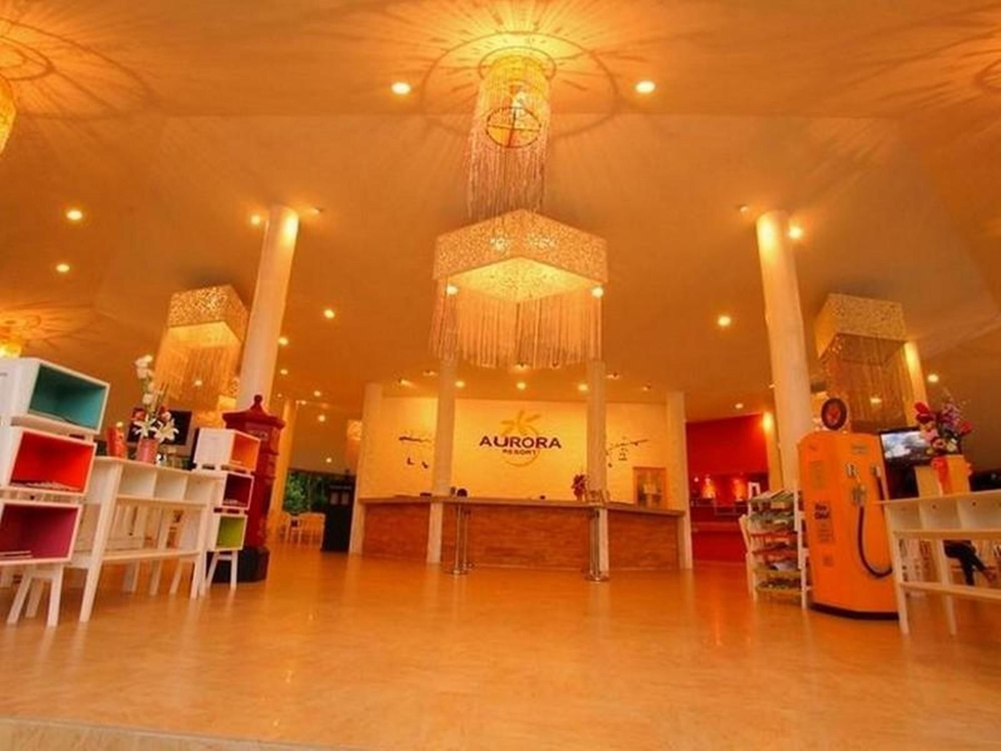A spacious lobby with a central reception desk labeled "AURORA," surrounded by modern shelving units and a high ceiling with decorative lighting fixtures.