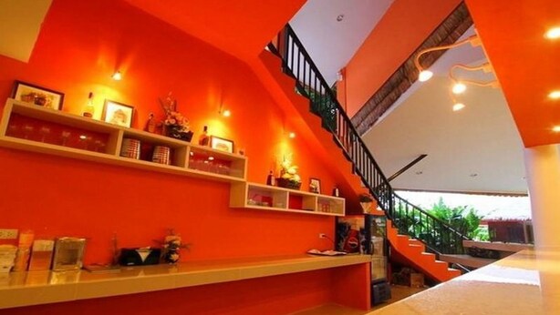 A modern interior with a bright orange wall, a staircase, and a reception desk with shelves. - Aurora Resort (Kanchanaburi)