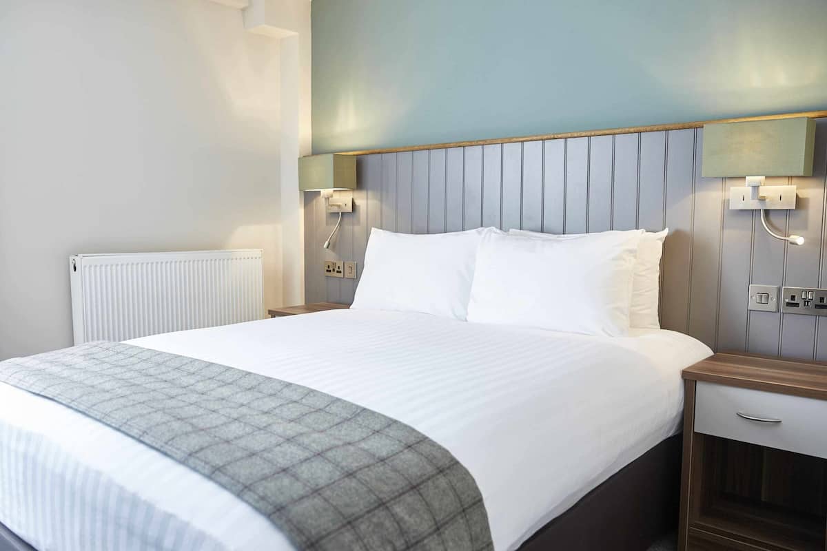 A hotel room with a bed, bedside tables, a radiator, and wall-mounted lighting.