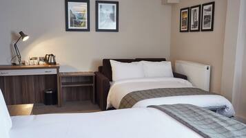 A hotel room with a bed, a desk with a lamp, a radiator, and framed pictures on the wall.