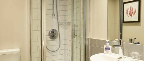 A modern bathroom with a glass-enclosed shower, a white sink, and a framed artwork on the wall.