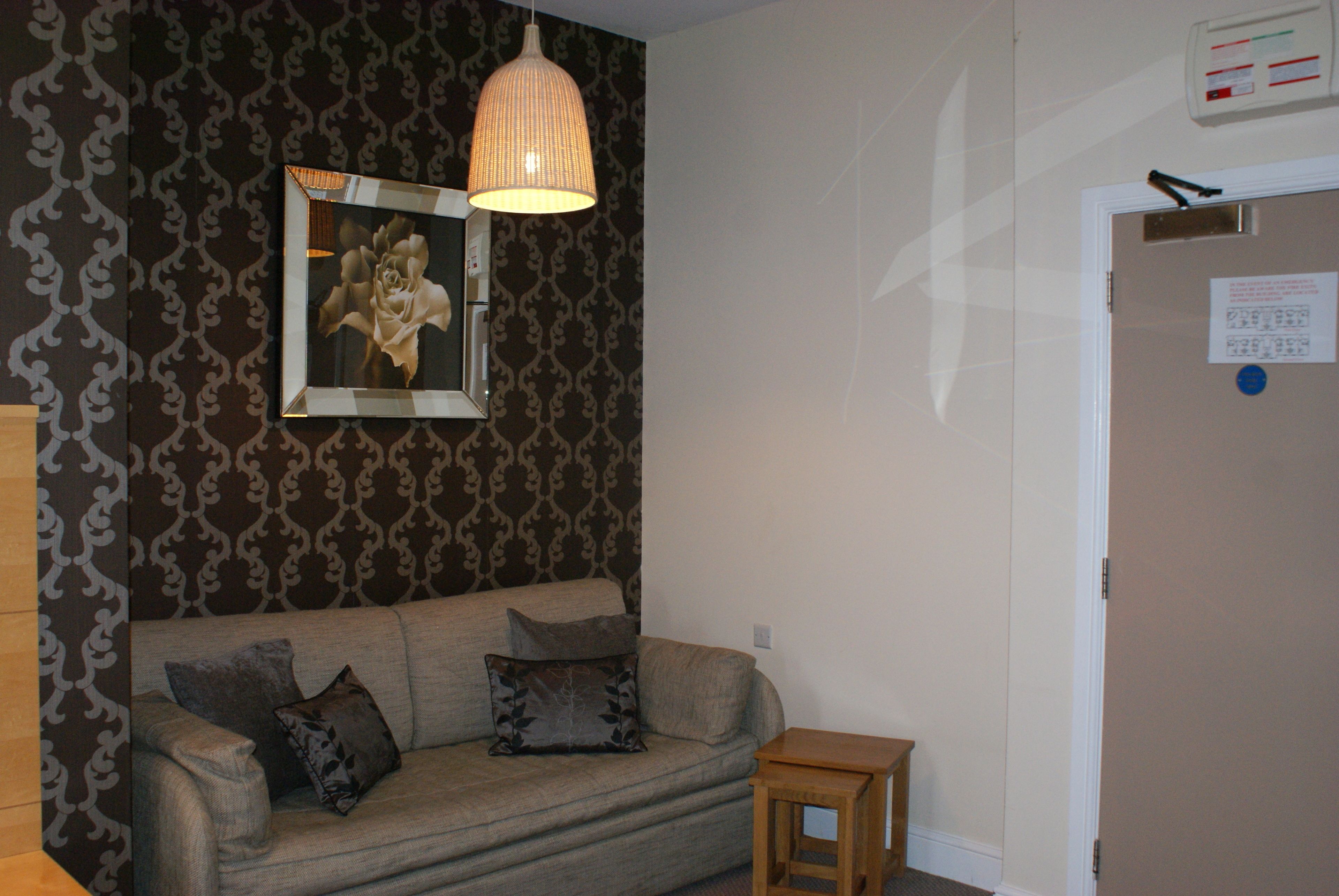 A living room with a patterned wallpaper, a sofa with cushions, a small wooden side table, and a hanging light fixture.